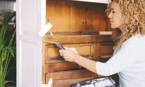 Kobieta maluje mebel z okleiny na biało wałkiem. Szuka inspiracji, jaka farba do mebli z okleiny będzie najlepsza.