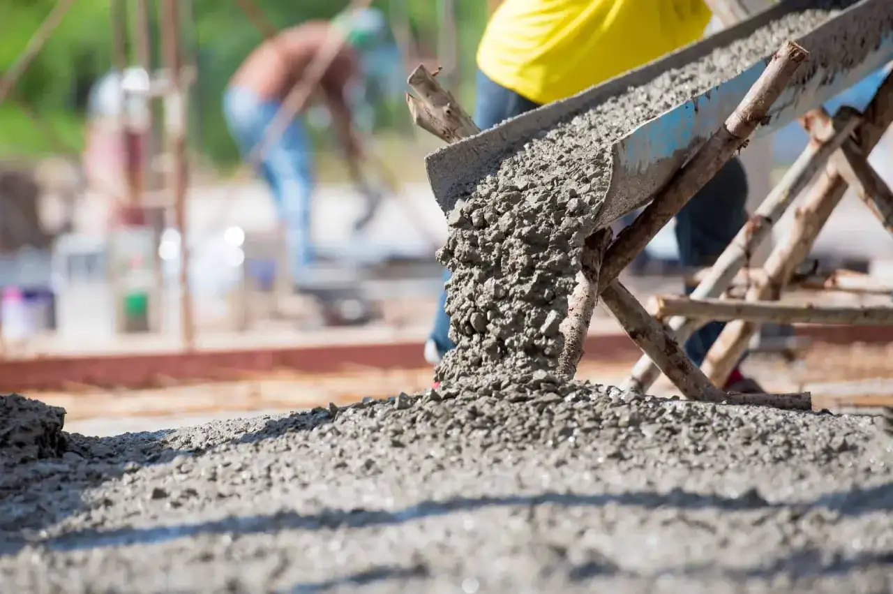Beton wylewany z rynny na placu budowy. Warto wiedzieć, ile waży kubik betonu, by zaplanować prace.
