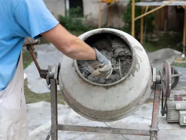 Mieszanie betonu w betoniarce. Zastanawiasz się, ile cementu na m3 betonu B20? Pracownik w rękawicach miesza masę.